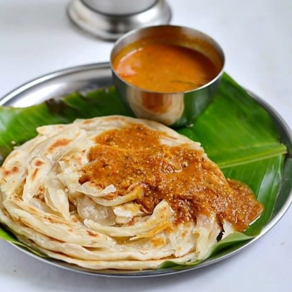 Flaky Indian parotta bread topped with a rich brown curry, served on a banana leaf.